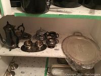 Shelf showing silver plated tall teapot, butter dish, 2 small lidded containers, silver salt and pepper shakers or small containers, smaller round tray.