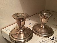 Two tarnished sterling silver candleholders shown standing on a surface with visible patina and wear.