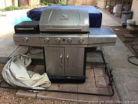 Full view of Char Broil stainless steel gas grill with 3 control knobs and side food warmer, includes grill cover folded beside it.
