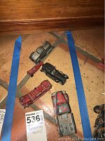 Top-down photo showing five vintage Tootsie Toy trucks arranged on terracotta tile floor with inventory sticker visible.