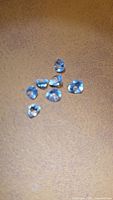 Seven light blue pear-cut gemstones on brown surface