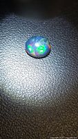 Black opal cabochon showing color play on textured surface