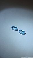 Two oval sky blue topaz gemstones on neutral background