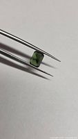 Octagon-cut green tourmaline held in tweezers, angled view