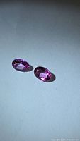 Two pink oval gemstones on white surface