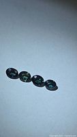Four oval-cut teal blue-green sapphires on neutral background