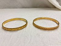 Two gold-tone Monet bangles side by side showing pattern differences