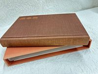 Book resting on slipcase showing brown cloth cover and spine