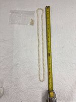 Full view of pearl necklace beside measuring tape and bag of loose pearls
