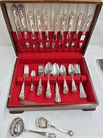 Full view of open wooden case showing knives in lid, forks and spoons in tray, serving pieces in front