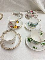 Six assorted floral teacup and saucer sets displayed on white cloth