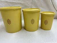 Three yellow Tupperware canisters side by side showing sizes and brown motif