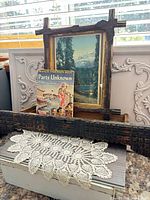 All four items grouped together: framed print, carved drawer front, paperback, crochet doily