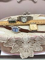 All four wristwatches on lace surface with ruler for scale