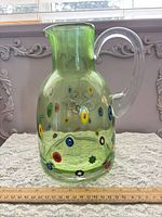 Full view of green glass pitcher with millefiori decoration next to ruler for scale