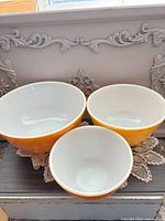 Three nested orange Pyrex bowls showing white interiors