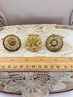 All three filigree gold-tone napkin rings or scarf clips arranged with ruler for scale