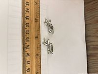 Pair of silver-tone floral rhinestone clip-on earrings beside ruler showing length