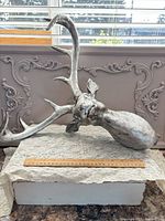 Full view of silver deer head sculpture with antlers and ruler for scale