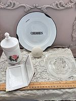 Group shot of all five items on lace cloth: enamel plate, glass juicer, rose jar, knob, photo wallet