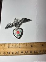 Front view showing RAF wing brooch and attached enamel heart locket with ruler for scale