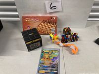 All seven items arranged: Rubik’s Impossible cube box, Chess Junior box, two cube puzzles, twist snake, star puzzle, Pikachu V card