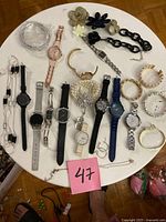 Overall lot view on round table showing watches, bracelets, necklace, brooches and hair clips