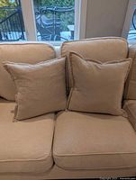 Two beige square pillows on sofa