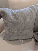 Front view of one grey woven pillow with size reference tag visible