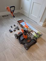 Mower deck with trimmer inserted, box and chargers visible