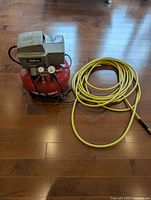 Porter Cable air compressor with coiled yellow hose on hardwood floor