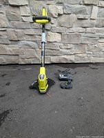 Full view of Ryobi string trimmer, battery attached, charger on ground
