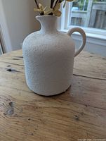 Side view of white textured ceramic jug vase with faux flowers