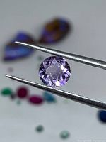 Front view of faceted round amethyst held in tweezers
