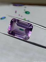 Emerald-cut amethyst held in tweezers showing clarity and color