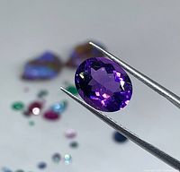 Amethyst held by tweezers showing bright purple color and faceting