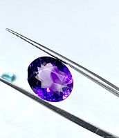 Front view of faceted oval amethyst held by tweezers