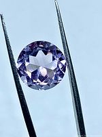 Front view of round faceted amethyst held by tweezers