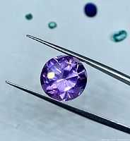 Round faceted light purple amethyst held by tweezers, frontal view