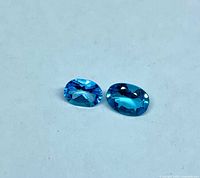 Two oval blue topaz gemstones on white background