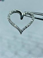 Front view of pendant held by tweezers showing diamond pavé and heart shape