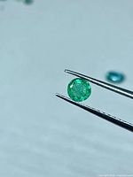Round green emerald held by tweezers, front view