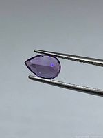 Side view of the pear-shaped purple amethyst held by tweezers