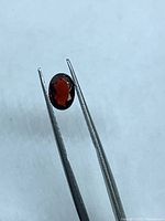 Garnet held by tweezers showing oval facet crown