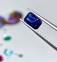 Blue emerald-cut sapphire held in tweezers