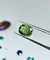 Peridot held in tweezers showing cushion cut and green color