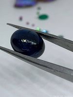Sapphire cabochon held in tweezers, showing deep blue color and dome surface