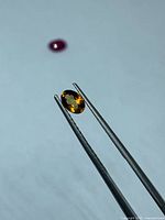 Citrine gemstone held in tweezers showing oval shape and colour