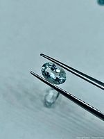 Close-up of one white topaz held by tweezers