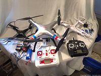 Three Syma quadcopters with controllers, batteries and cables displayed on table